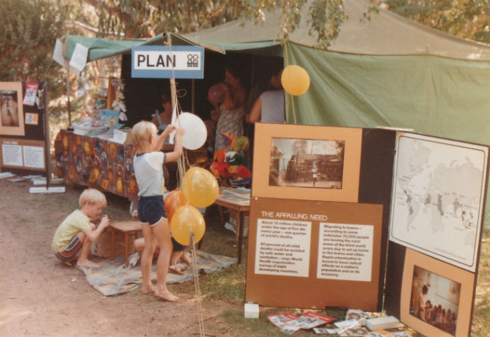 Children help their parents set up a Friends of Plan advocacy stand at Sunday in the Park in Canberra in the 1980s