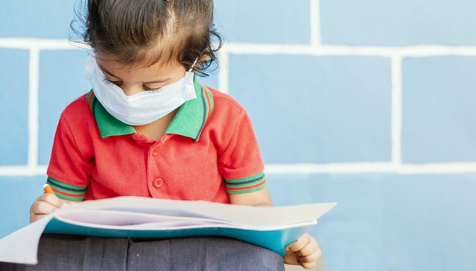 Young girl wears face mask while drawing picture