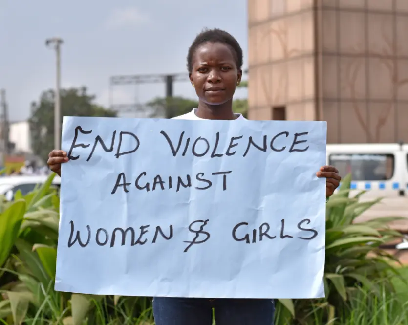 A girl stands in Kampala, Uganda holding a handmade sign that says “End Violence Against Women and Girls”