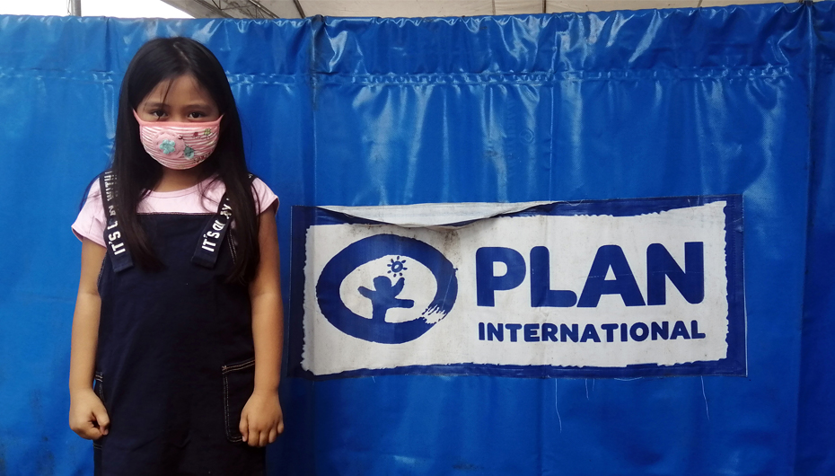 Girl in Philippines in front of Plan International sign