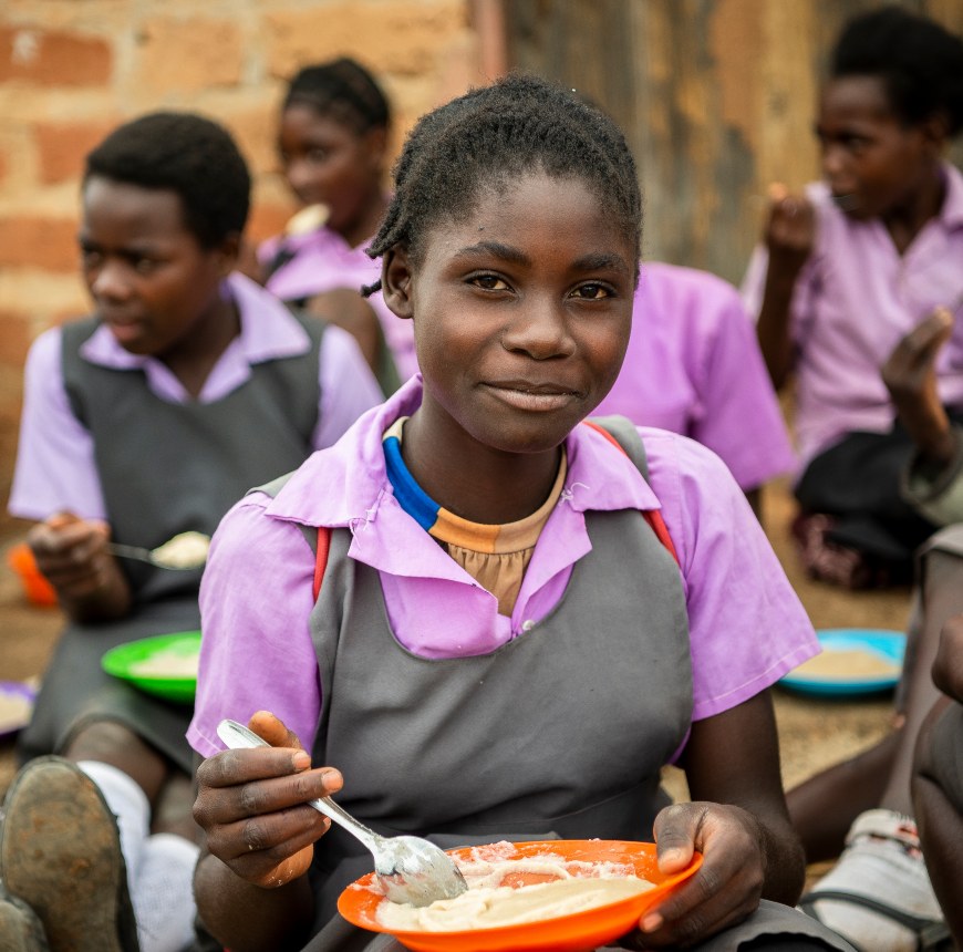 Girl eats lunch at her school provided as part of the School Feeding Programme