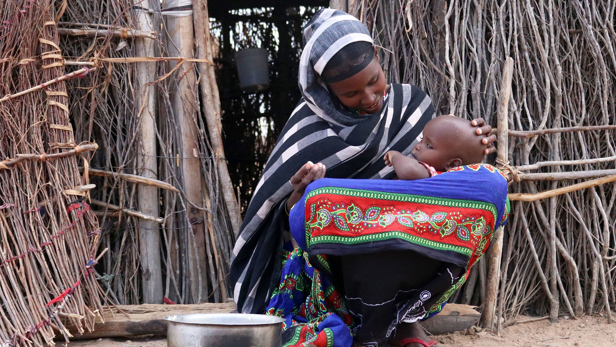 Mother cradles her baby in front of a temporary shelter made from small branches