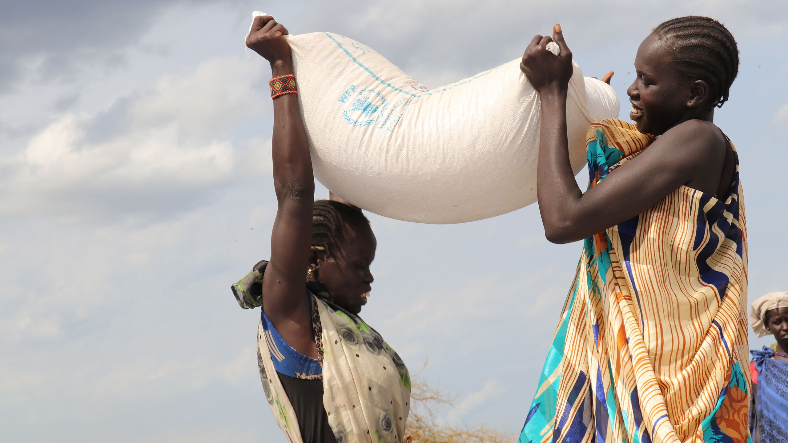 Two women lift a World Food Program supplied bag of grain