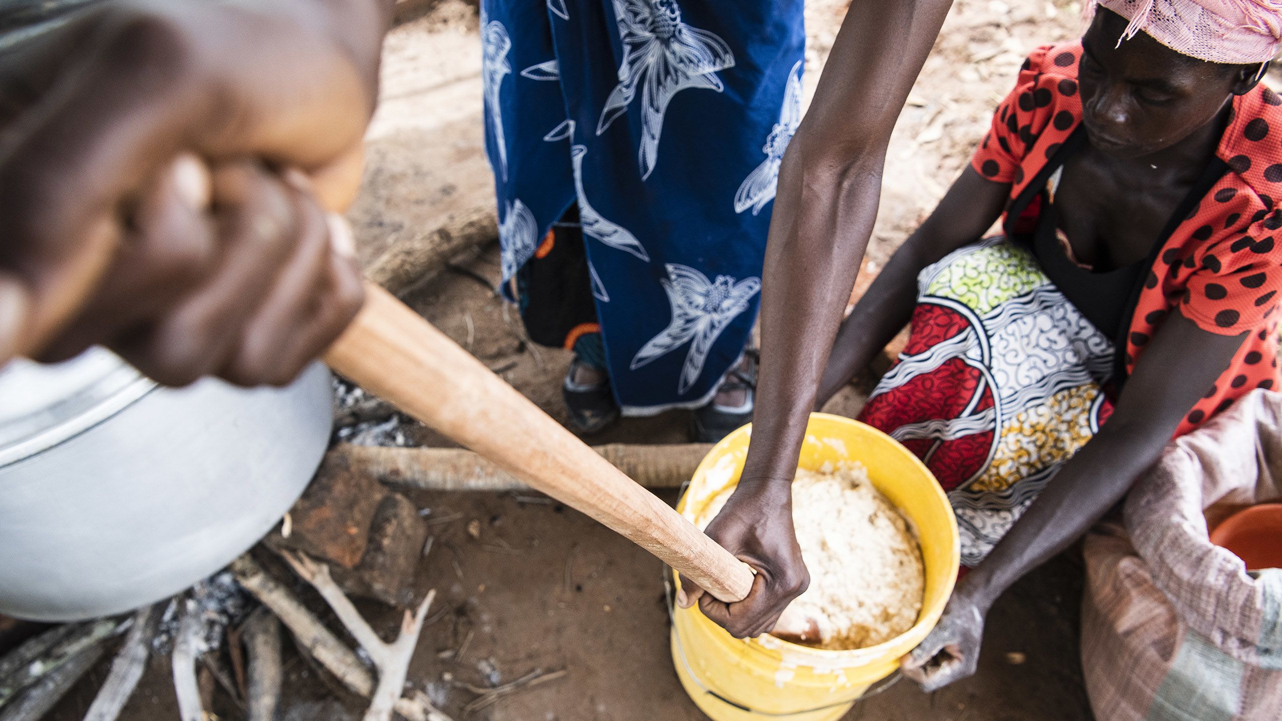 Women prepare a school meal, mixing a paste in a large container.