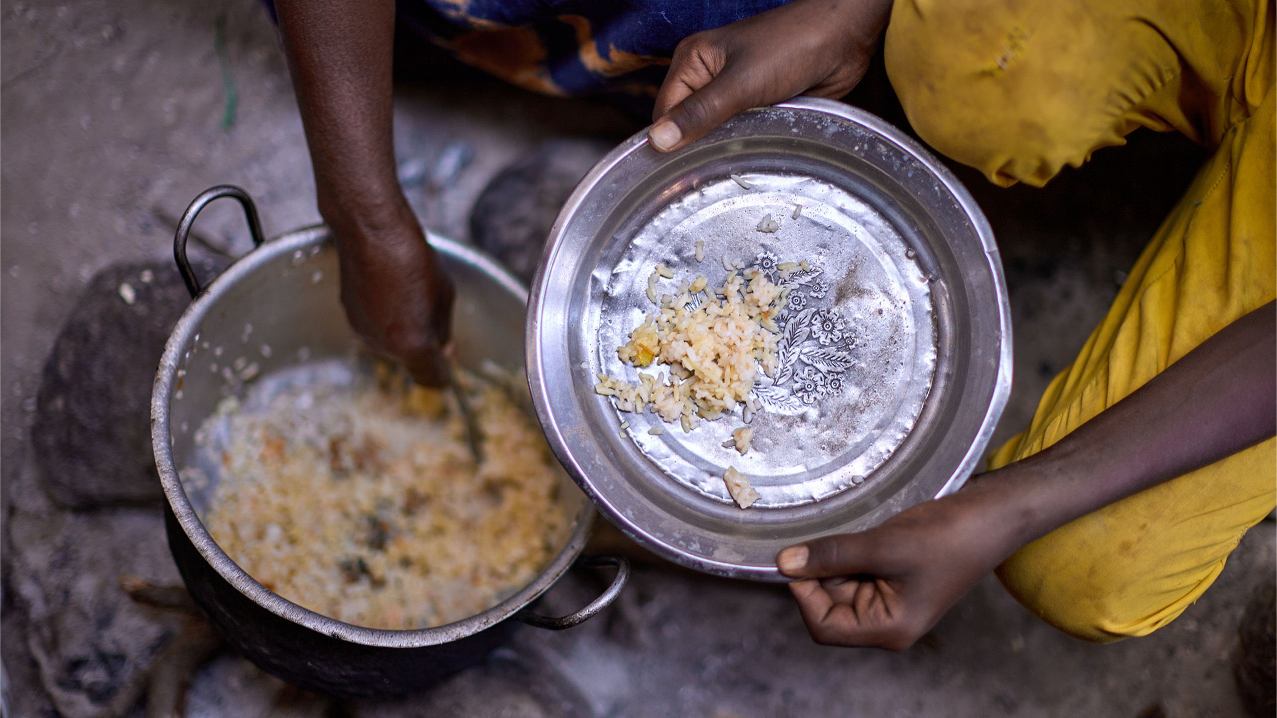 A mother spoons rice onto a silver plate.