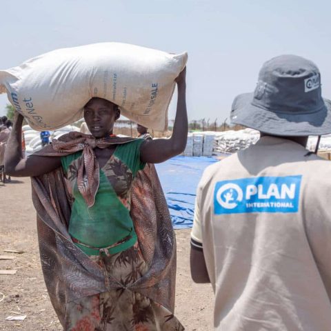 Woman carries home sack of sorghum on her head from food distribution point